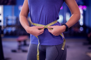 Woman measuring waist with meter in the gym. People, fitness and health concept