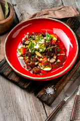 Warm beef liver salad with arugula, lettuce and tomatoes on a red plate. A delicious gourmet dinner in the rustic style