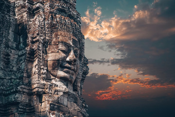 The Bayon - Khmer temple at Angkor Wat in Cambodia. Popular tourist attraction. Smiling stone faces on the towers of temple. Dramatic sky. - obrazy, fototapety, plakaty