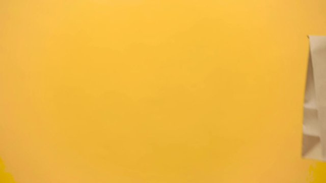 Close up female hold in hand brown clear empty blank craft paper bag for give takeaway isolated on yellow background. Packaging template mock up. Delivery service concept. Copy space. Advertising area