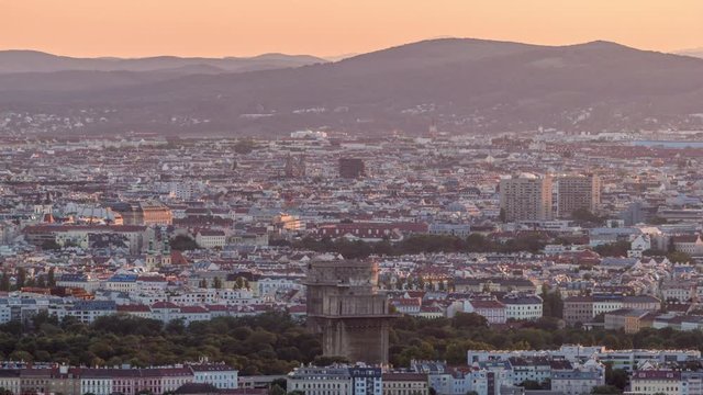 Aerial panoramic view of Vienna city with skyscrapers, historic buildings and mountains on a background timelapse in Austria. Evening skyline before sunset from Danube Tower viewpoint