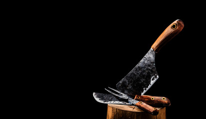 Rustic butcher meat knife, cleaver and fork on black background