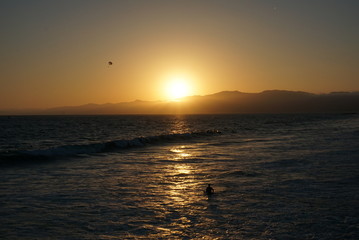 Sun going down behind a surfer and Paraglider off the beaches of Santa Monica, California