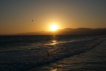 Sun going down behind a surfer and Paraglider off the beaches of Santa Monica, California