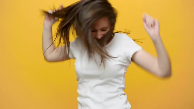 Smiling pretty fun crazy happy brunette young woman in white t-shirt fooling around dancing circling jumping smile isolated over yellow background in studio. People sincere emotions lifestyle concept.