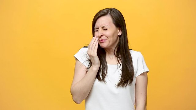 Tired fatigued exhausted brunette young woman in striped shirt keeping eyes closed, putting hand on nose, yawning isolated over yellow background in studio. People sincere emotions, lifestyle concept.