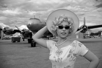 Woman in retro outfit in front of antique propeller airplane