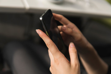 Young business woman uses phone. Good looking brunette female uses online banking on smart phone to transfer money from credit card. Girl using smart phone and chatting with business partners in cafe.