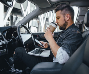 Young handsome driver man with laptop serfing internet and drink black coffee