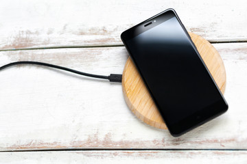 Concept of modern technologies. The black smartphone is on a wireless charger. White wooden background with horizontal stripes. Copy space. Flat line