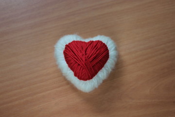 Red and white heart of thread on a wooden background.