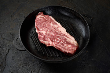 fresh raw marbled beef steak in a pan on a dark background