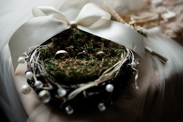 Wedding rings on the decorated nest with greenery and white ribbon