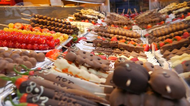 Various fruits on a wooden skewer stick in a caramelized glaze made of milk black white chocolate. Grapes, banana, strawberries in icing on the counter of the Christmas market