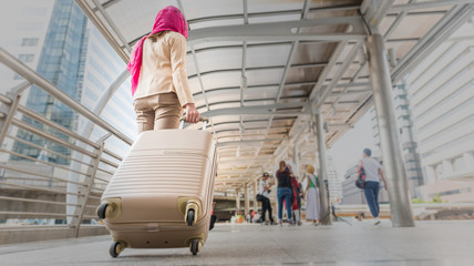 Back view of Muslim traveler woman walking and carrying a suitcase in a travel location on holidays or business trip, traveling concepts. 