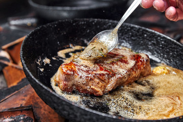 frying pan on a stove on which a large piece of meat is fried with butter