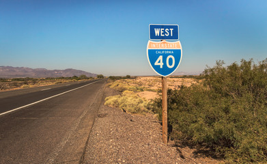 highway sign in the middle of desert road on a sunny day