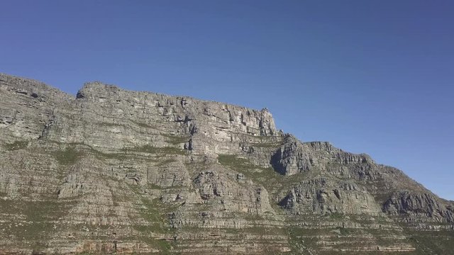 Aerial lower angle scenic drone flight view of Table Mountain in late afternoon sun against blue sky. Steep sand stone cliff and tectonic lines. steady shot with copy space.