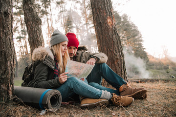 Travel couple camping with map in the forest. Concept of trekking, adventure and seasonal vacation.