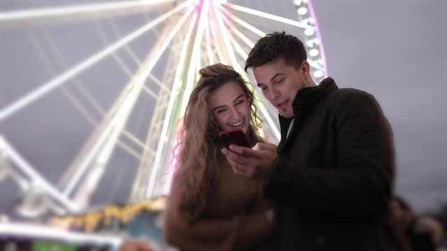 Happy couple having fun at amusement park and looking at mobile phone
