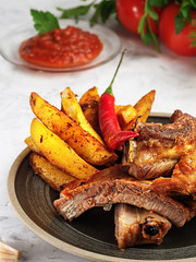 Grilled ribs with French fries and vegetables on the grey background. Shallow depth of field. Vertical orientation.