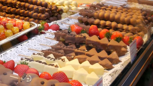 Various fruits on a wooden skewer stick in a caramelized glaze made of milk black white chocolate. Grapes, banana, strawberries in icing on the counter of the Christmas market