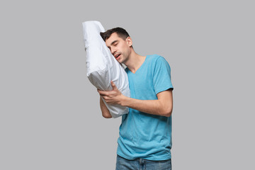 Tired brunet man in a blue tee resting on a white pillow isolated over grey background.
