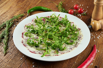 Veal carpaccio with parmesan, rucola and truffle oil on a white plate in a composition with spices on a wooden background Italian cuisine. Salad, antipasti