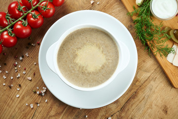 Mushroom cream soup with champignons, garnished with fried mushrooms, olive oil and grated Parmesan cheese in grey bowl on a wooden background. Healthy diet. Top view food