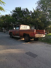 Camioneta roja vieja estacionada en la calle rodeado de árboles mientras amanece