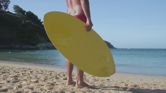 Skimboarder stands on the beach and holds his board