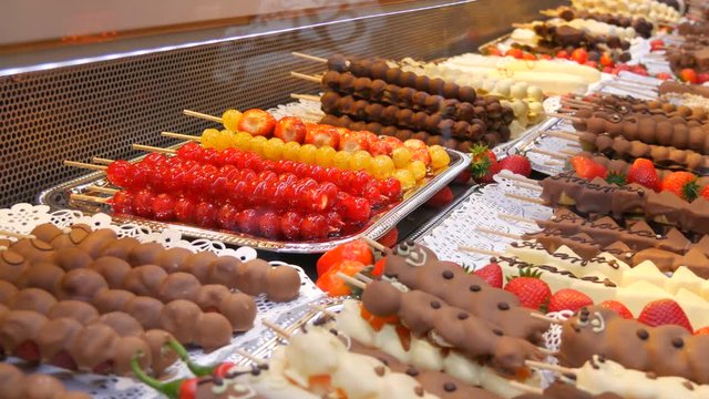 Various fruits on a wooden skewer stick in a caramelized glaze made of milk black white chocolate. Grapes, banana, strawberries in icing on the counter of the Christmas market