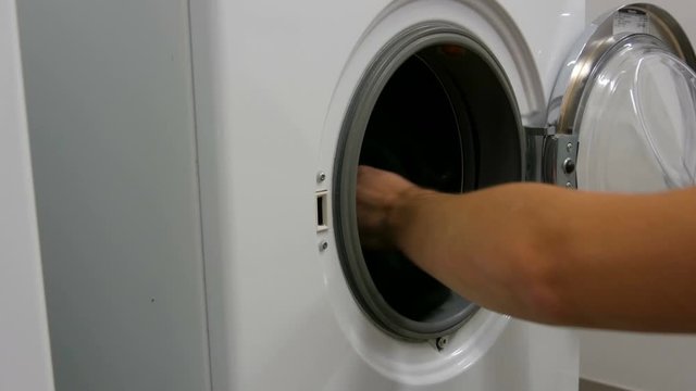 Men hands loads laundry and clothes into the washing machine. Large white washing machine in the laundry room.