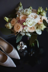 Beautiful bouquet of fresh roses, peonies, eucalyptus flowers in pastel pink and cream colors and other bridal accessories. Wedding rings, bridal bouquet, and bridal shoes before the wedding ceremony.