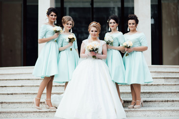 Bridesmaids in turquoise dresses are standing near the bride and groom outdoors. Beautiful girls on wedding day posing on the stairs. Elegant friends with bouquets. Autumn. Wedding.