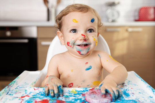 Laughing baby in high chair with finger paint on face and body