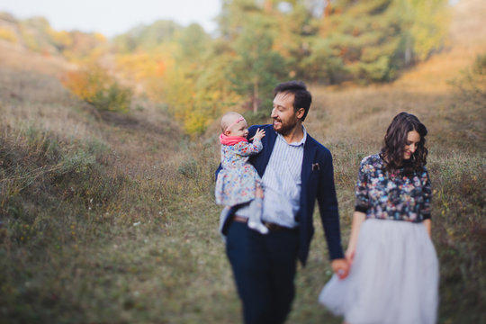 Young happy caucasian couple with little baby girl. Parents and daughter walking and having fun together. Mother and father play with child outdoors. Family, parenthood, childhood, happiness concept.