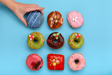 Various colorful donuts on blue background, female hand takes a donut. Top view.