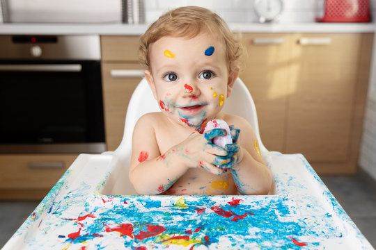 Cute baby in high chair with finger paint on face and body