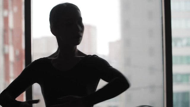 Silhouette. Ballerina in a black tutu dancing ballet in the background of the window and the city. Slow motion. Steadicam shot Close up