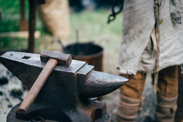 The hammer lies on the anvil in the forge. A craftsman forges metal. A blacksmith in old work clothes.