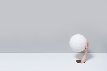 Hand in the hole. A kid hand holds a white volleyball ball on grey and white background