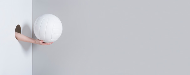Hand in the hole. A kid hand holds a white volleyball ball on grey and white background