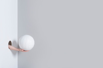 Hand in the hole. A kid hand holds a white volleyball ball on grey and white background