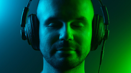 A young man is enjoying music with headphones. His eyes are closed. Blue and green color theme.