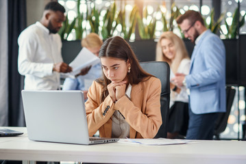 Young business woman working at office table in front of laptop suffering from headache feeling tired after hard workday.