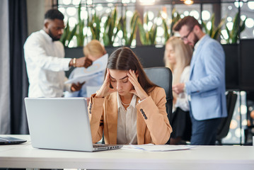 Young business woman working at office table in front of laptop suffering from headache feeling tired after hard workday.