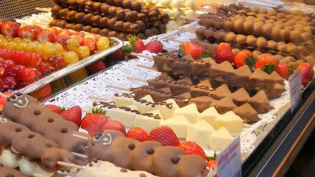 Various fruits on a wooden skewer stick in a caramelized glaze made of milk black white chocolate. Grapes, banana, strawberries in icing on the counter of the Christmas market