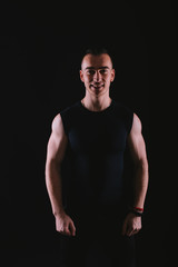 Portrait of happy young fitness trainer standing over dark background in studio