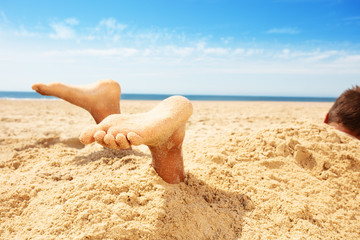 Legs and feet boy covered by sand in a game on sea